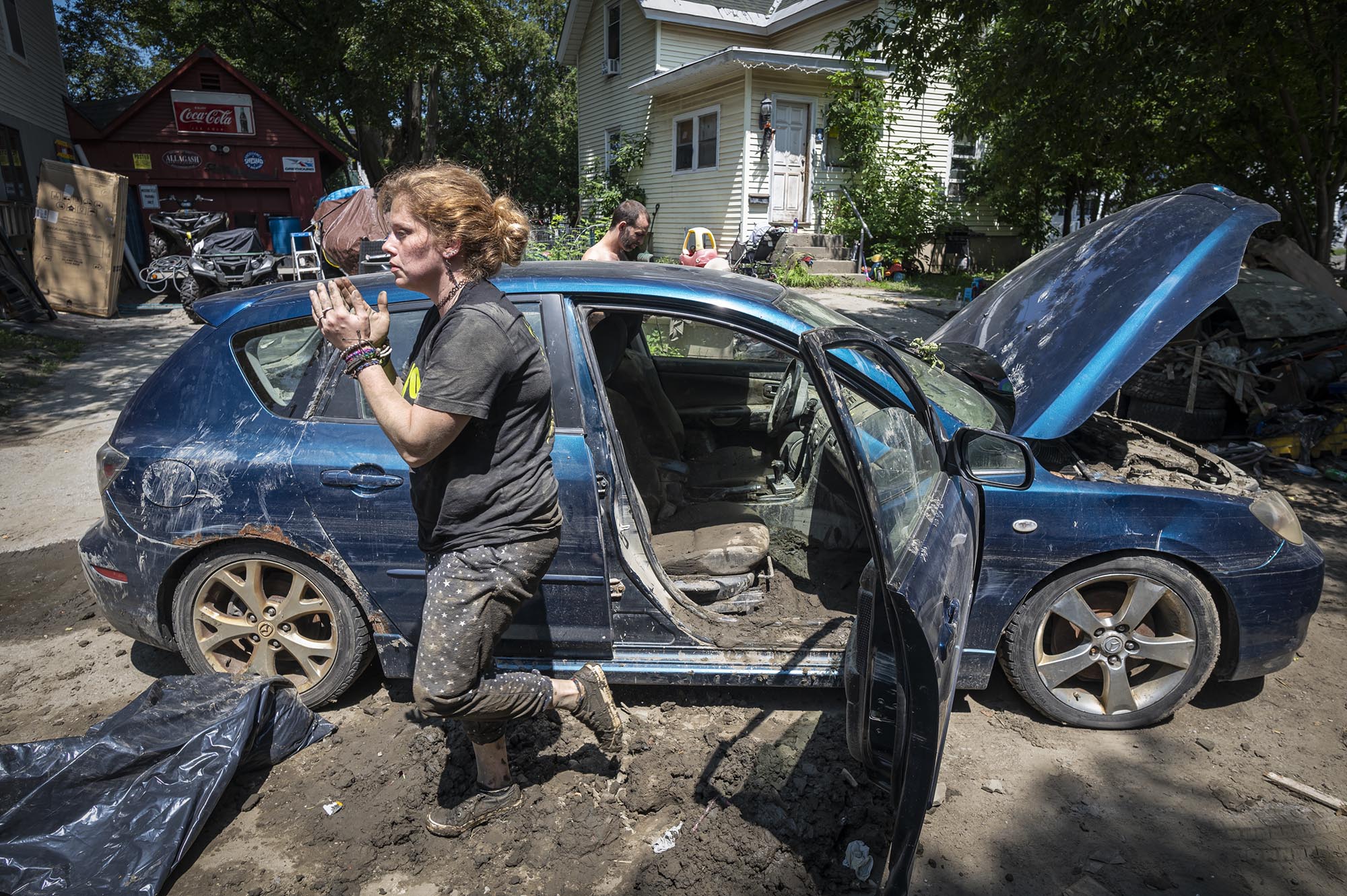a woman is standing next to a blue car in the mud.