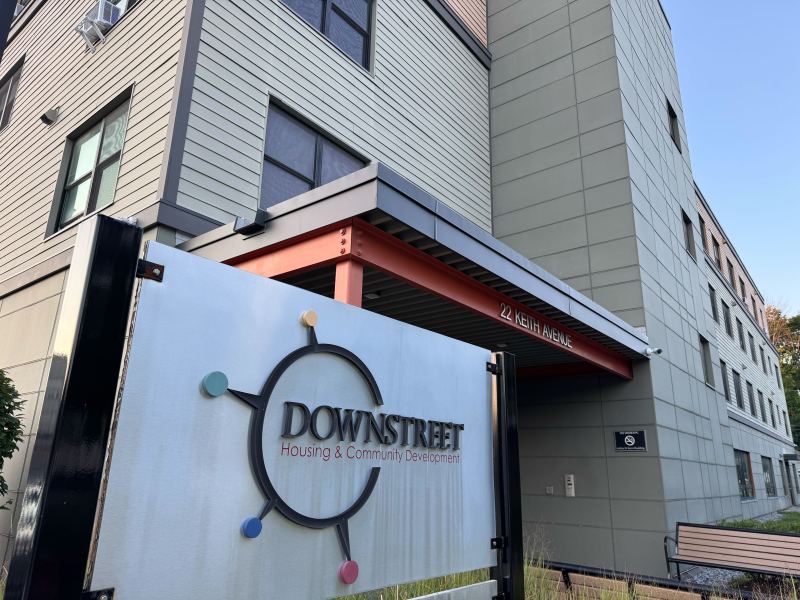 A sign reading "Downstreet Housing & Community Development" stands in front of a modern multi-story building at 22 Keith Avenue.