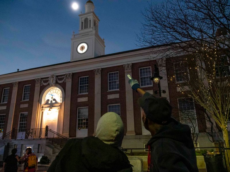 People standing outside a building at dusk with one person pointing towards the clock tower.