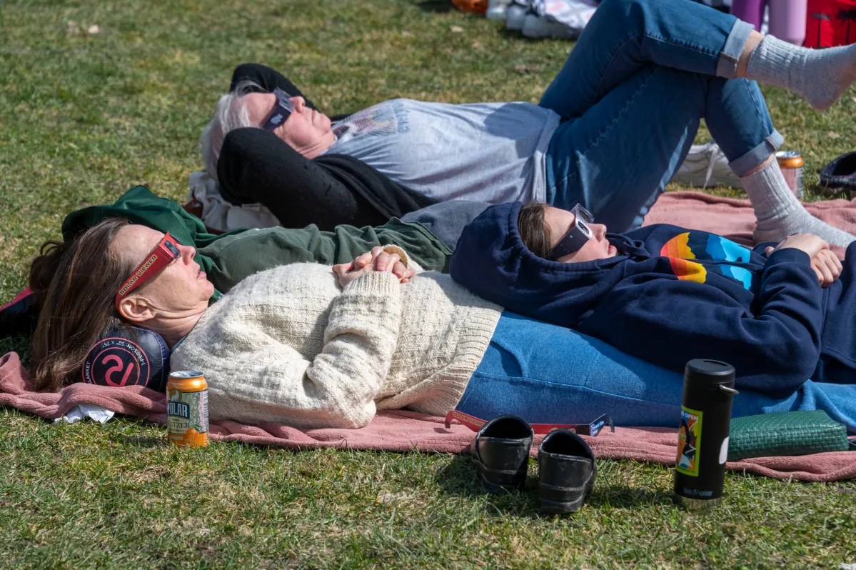 Three people relaxing on a blanket outdoors with drinks nearby.
