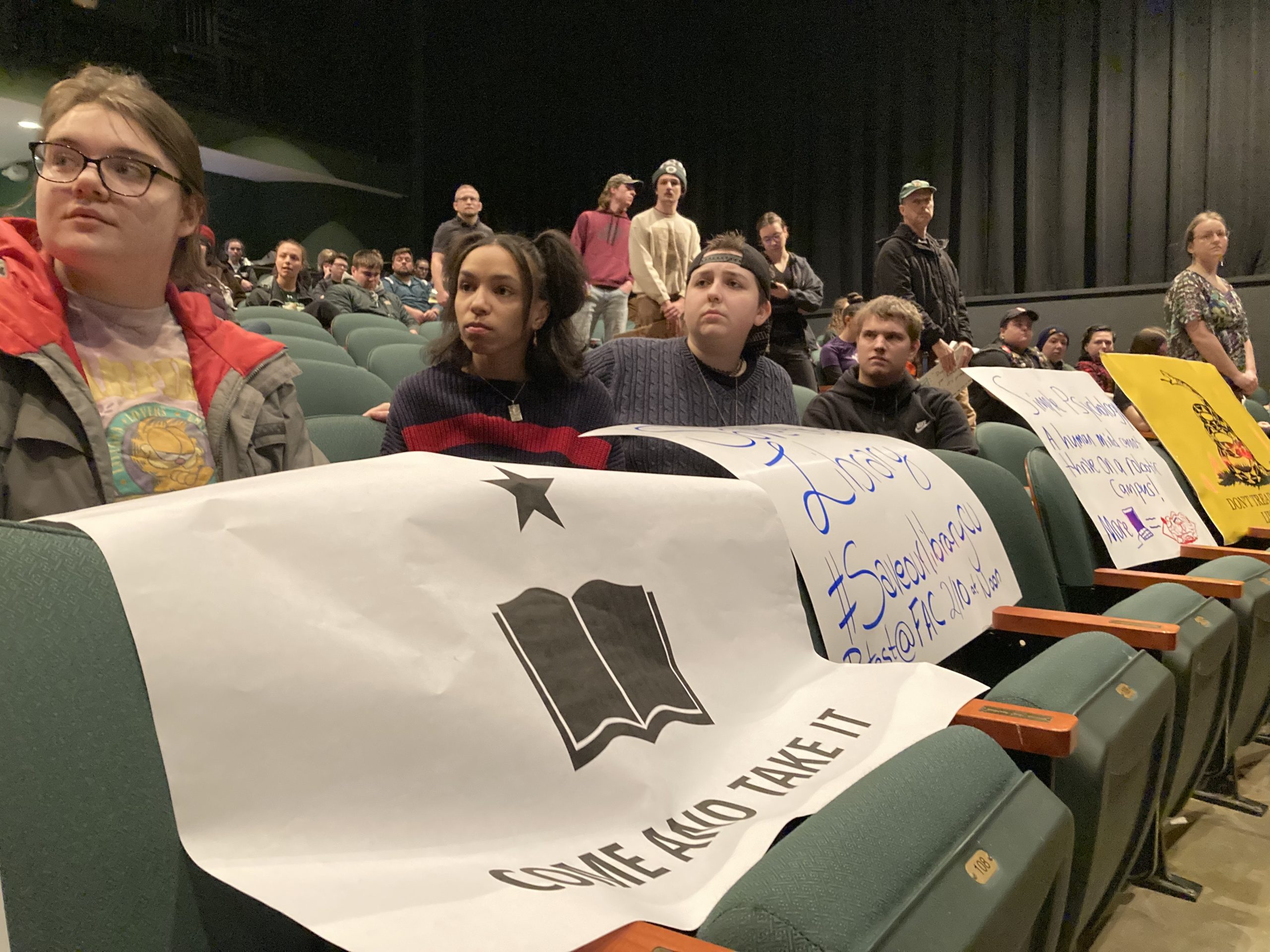 a group of people sitting in a theater holding signs.