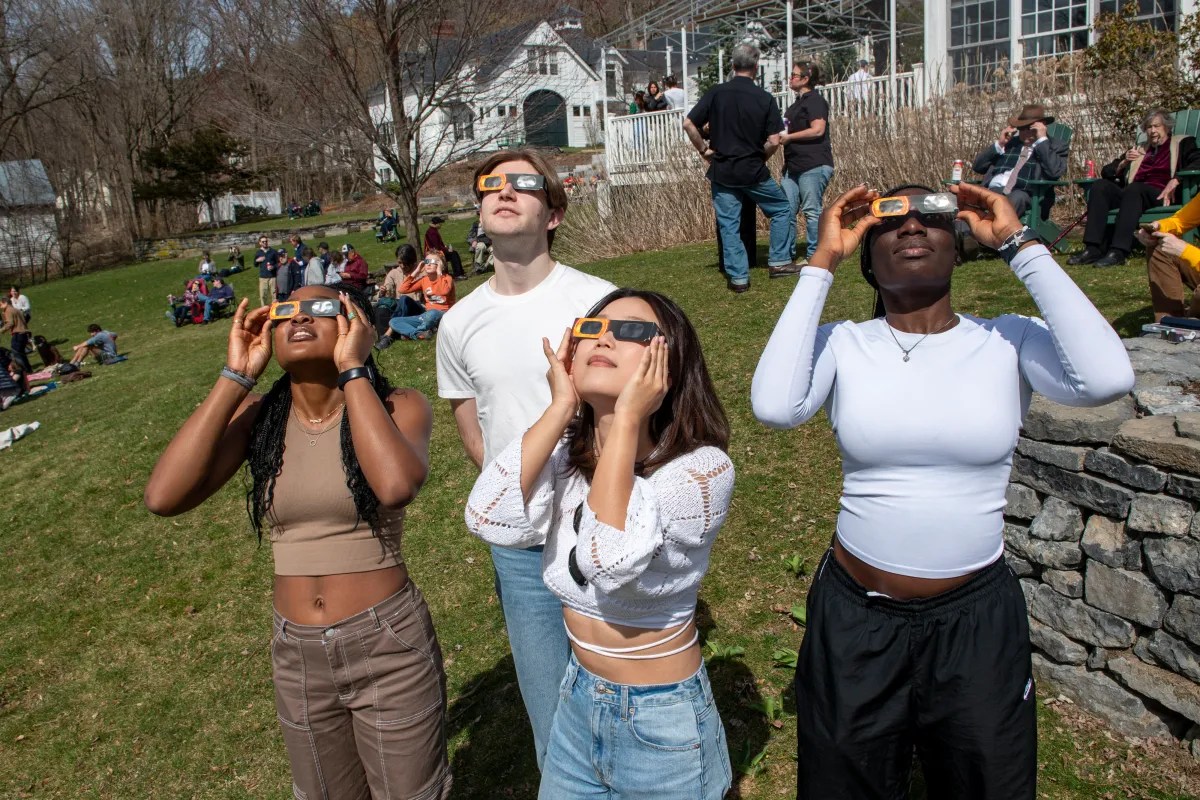 Group of people wearing protective glasses looking upwards at a solar eclipse.