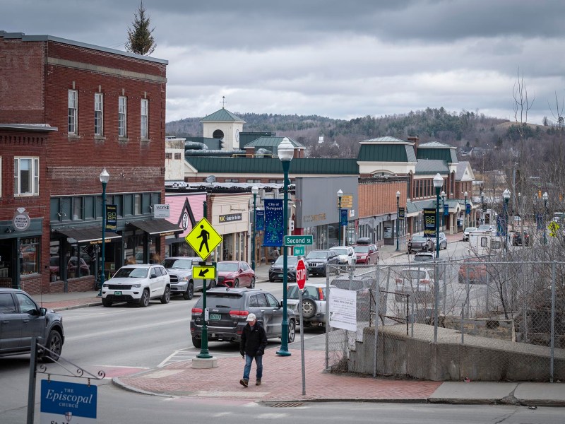 A cloudy day on a small town main street with pedestrians and vehicles, featuring a mix of traditional and modern architecture.