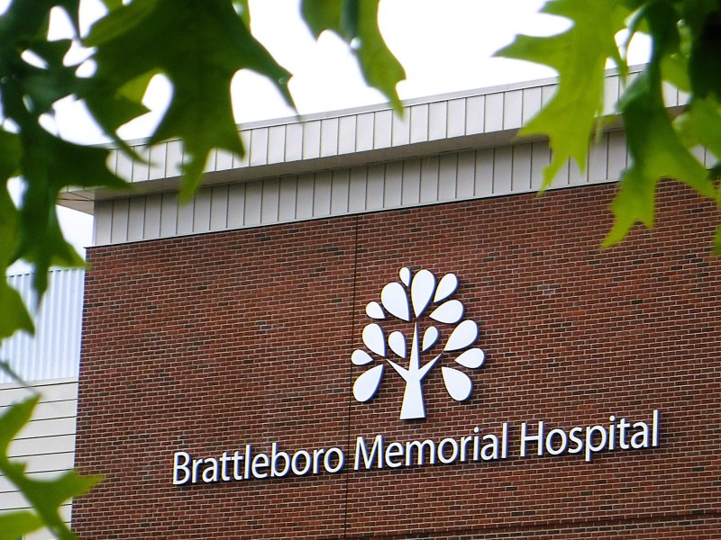 The exterior sign for Brattleboro Memorial Hospital is displayed on a brick building, partially framed by green leaves.